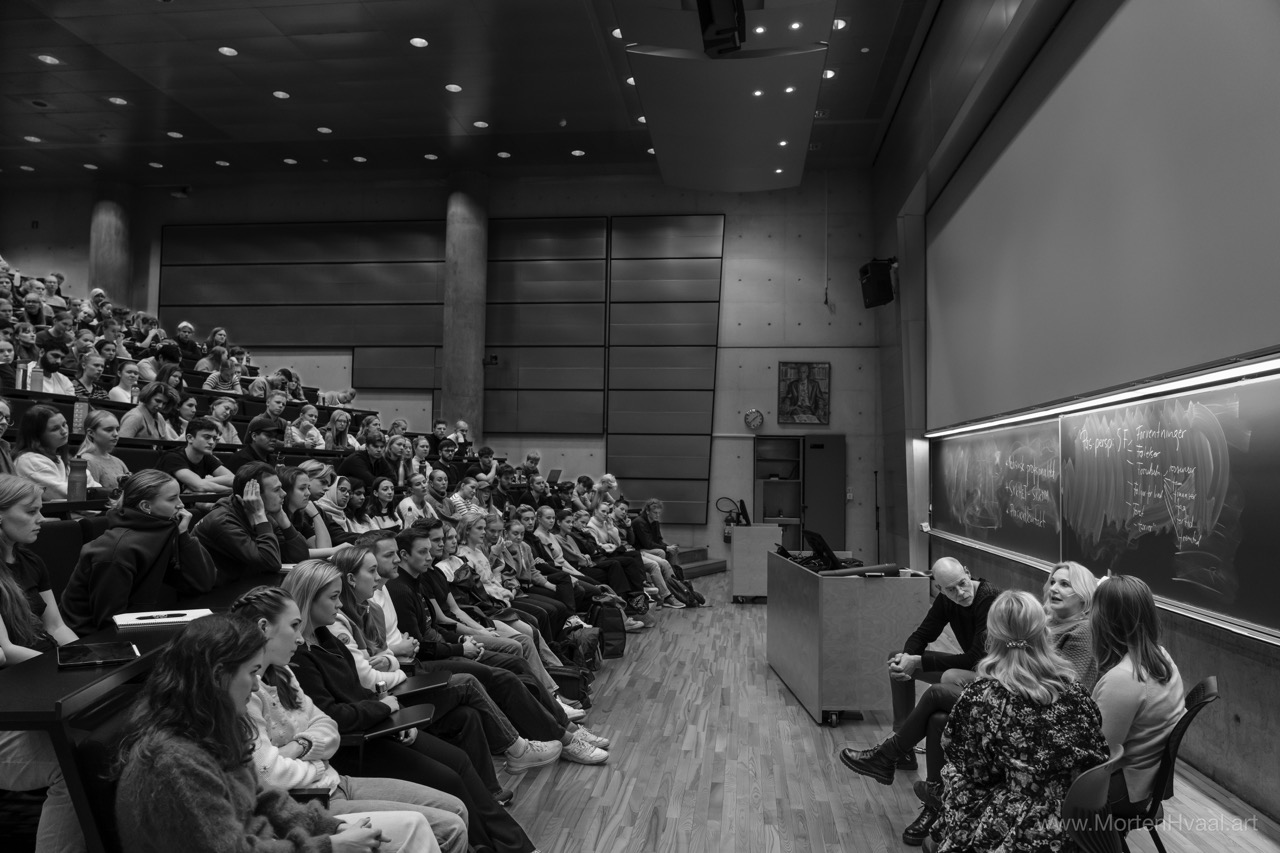 Studenter i auditorium som følger panel foran tavle.